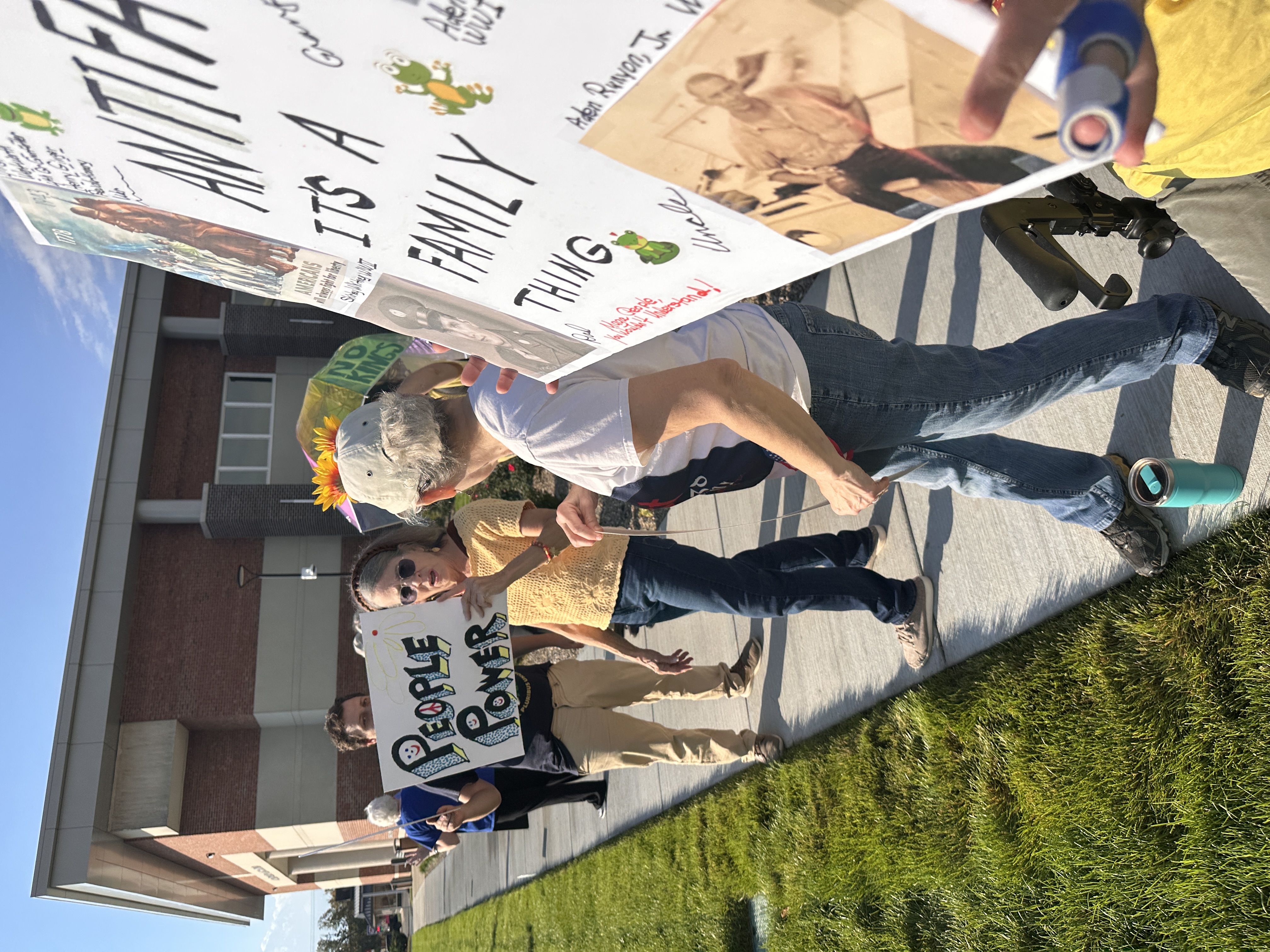 Close up of protestors holding signs that read People Power and "Antifa, It's a Family Things" with photos of WW1 and WW2 veterans from their family during No Kings Day 2.0