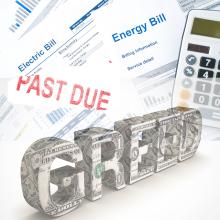 Image with "Greed" written as currency over utility bills, past due stamp and calculator